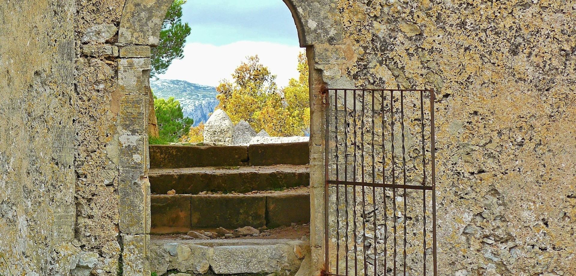 Durch eine große, karge, triste Steinmauer führt ein kleines, geöffnetes Tor in eine wunderschöne, sonnenerhellte Landschaft hinein